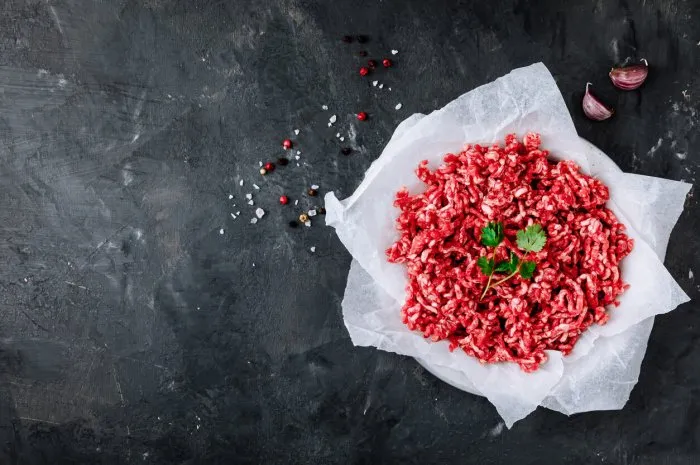raw ground minced meat and seasonings on dark background, top view, copy space