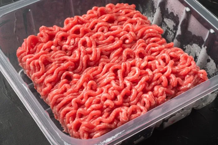 ground beef in plastic tray with raw minced homemade meat set, on black stone background