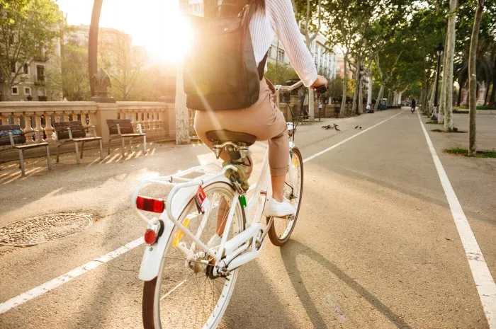 cropped back view image of young lady outdoors walking on bicycle on the street