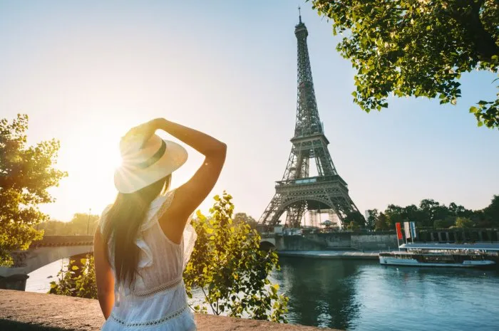 young woman tourist in sun hat and white dress standing in front of eiffel tower in paris at sunset travel in france, tourism concept high quality photo