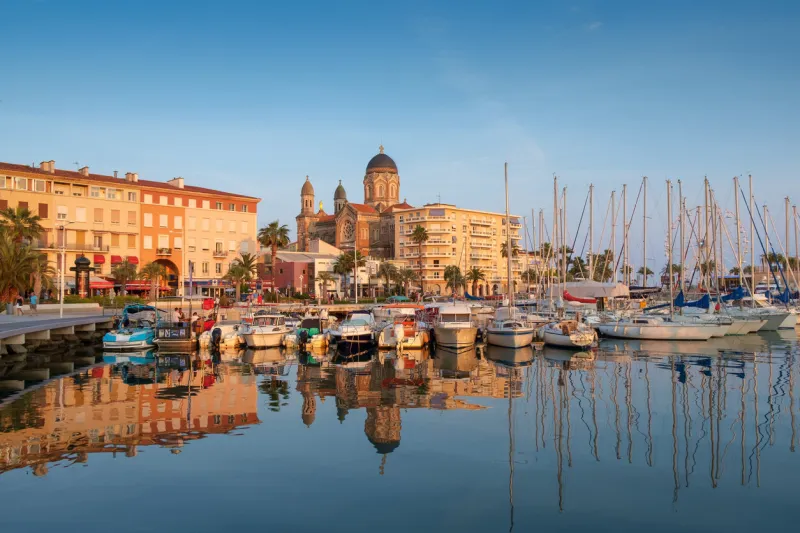 the seafront of saint raphael in the evening sun, with the basilica overlooking the streets, shops and marina the scene is reflected in the calm water of the mediterranean
