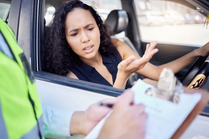 shot of a young businesswoman looking upset at receiving a ticket from a traffic officer