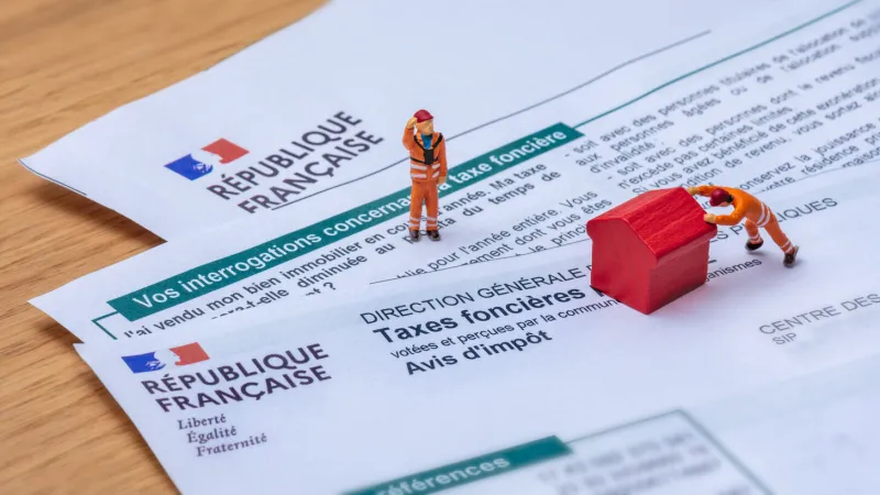 clamart, france - 6 septembre 2022   détail d'un avis d'impôt français sur les taxes foncières avec de petits personnages déplaçant une maison jouet rouge en bois