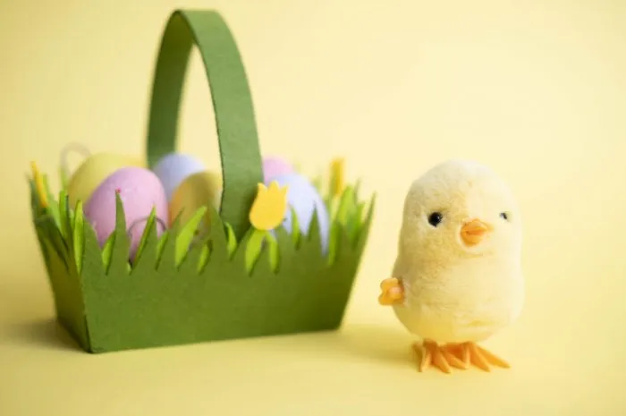 easter card a small yellow toy chicken, next to a green basket with colorful eggs, on a yellow background we are celebrating easter