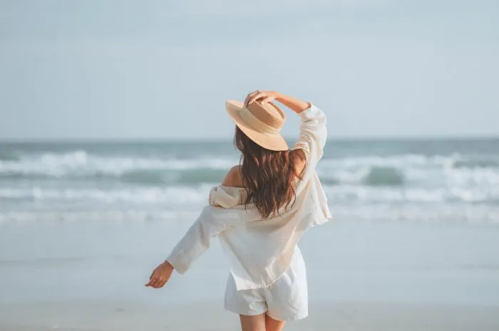 summer beach vacation concept, young woman with hat relaxing with her arms raised to her head enjoying looking view of beach ocean on hot summer day, copy space