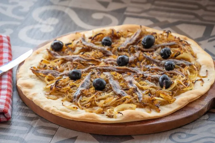 a cooked pissaladière pie, in close-up on a wooden board