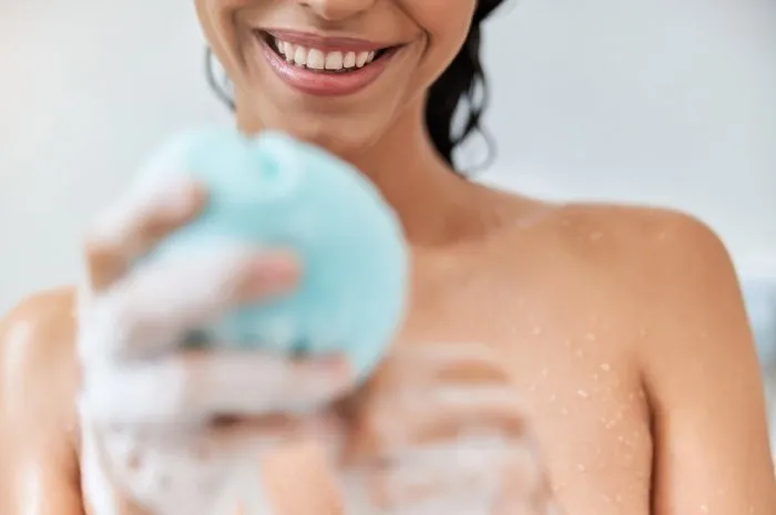close up of smiling lady with bath washcloth in her hand taking shower at home