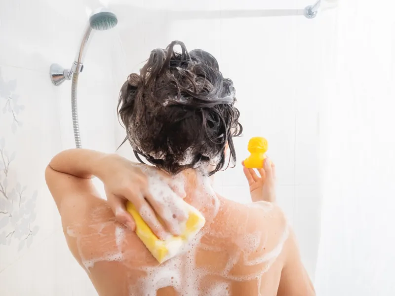 naked woman with short hair takes a shower woman washes her hair with shampoo yellow rubber duck on girl's palm in white bathroom