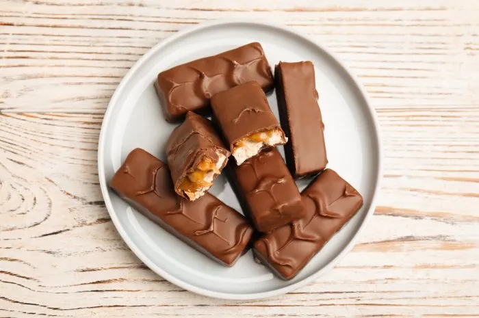 plate of chocolate bars with caramel, nuts and nougat on white wooden table, top view