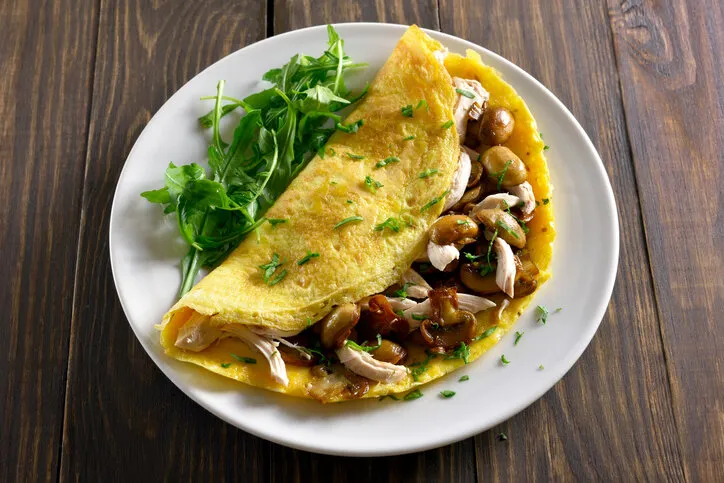 close up of omelet filling with mushrooms, chicken meat, greens on wooden table healthy food for breakfast close up view