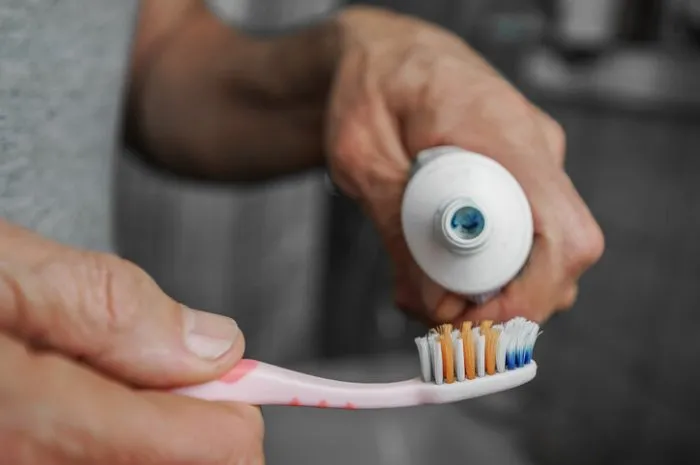 old man with wrinkled hands squeezing paste to toothbrush close up view dental health care and hygiene concept