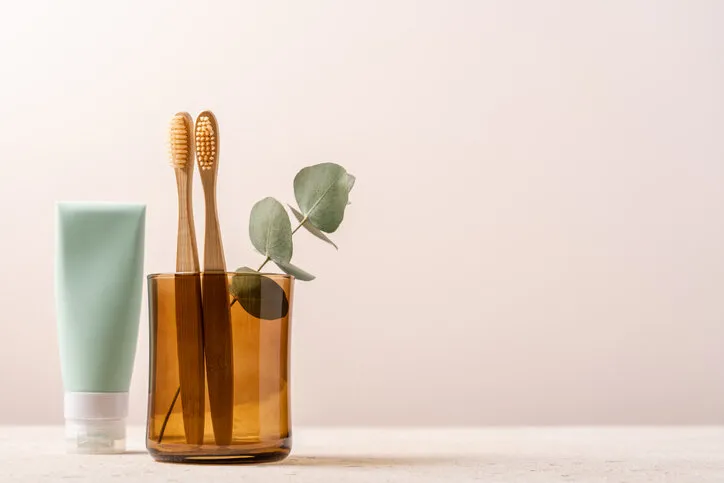 bamboo toothbrushes in glass and tube of toothpaste on light background