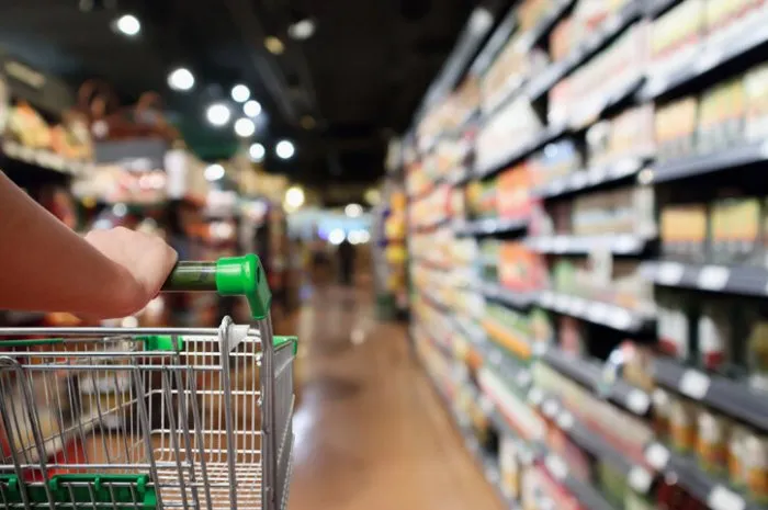 woman hand hold shopping cart with abstract blur supermarket aisle background