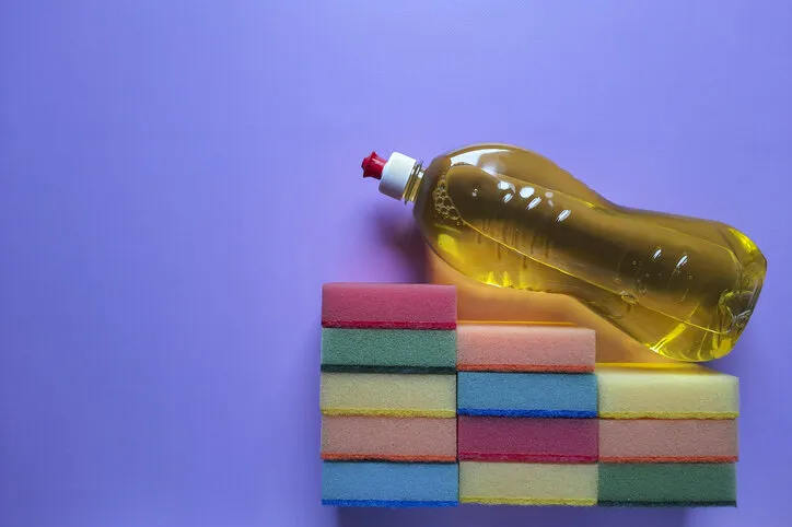 bottle of yellow detergent on kitchen cleaning sponges, folded in form of steps purple background with place for text