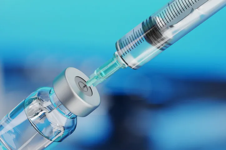 medical disposable syringe for vaccine injection and glass vial on blue blur background