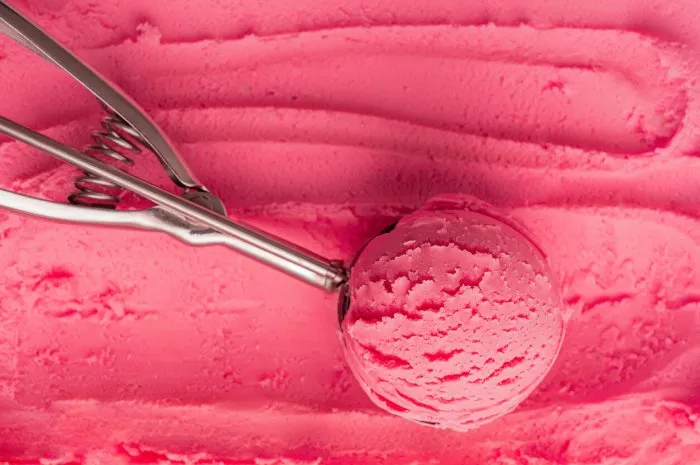 high angle view of scoop of pink cold sweet ice cream or sorbet made with juicy red berries, raspberry or strawberry in metal silver serving spoon on textured gelato background refreshing natural dessert