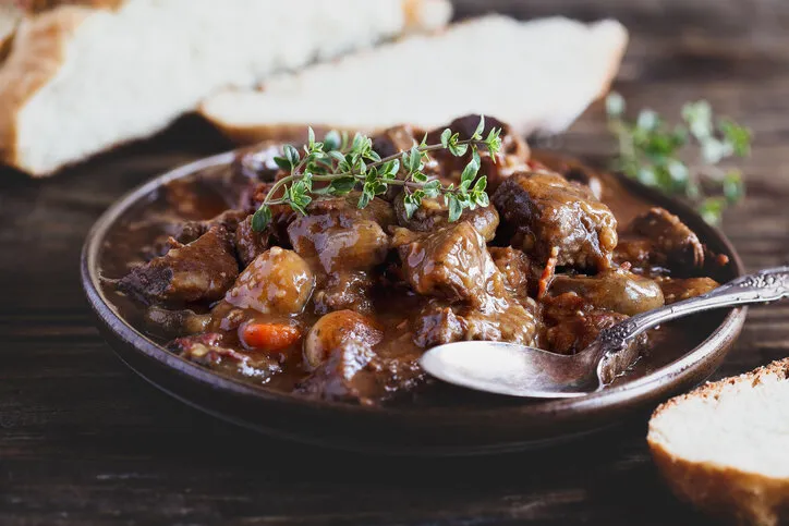 bowl of beef bourguignon or boeuf garnished with fresh lemon thyme and served with homemade artisan bread over a rustic wood background table