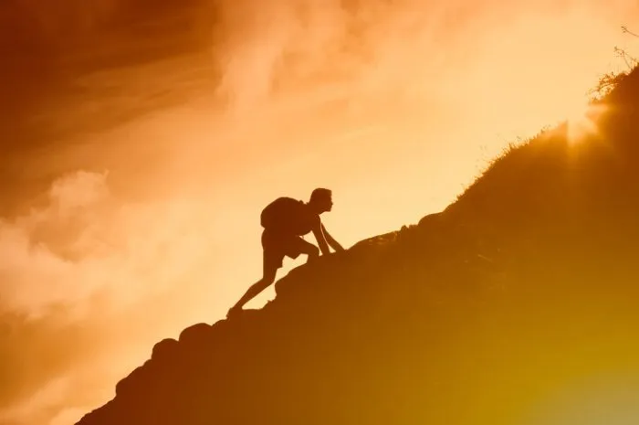 man climbing up mountain cliff working hard to reach goals