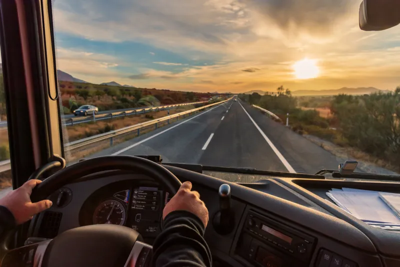 view from the driver's seat of a truck of the highway and a landscape of fields at dawn, with a dramatic sky