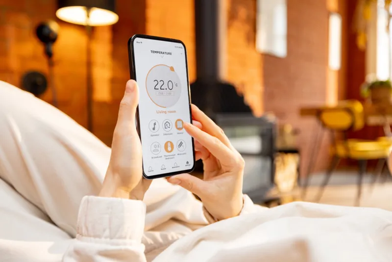 woman holding phone with running smart home application for heating temperature control, while lying relaxed at home close-up on device screen