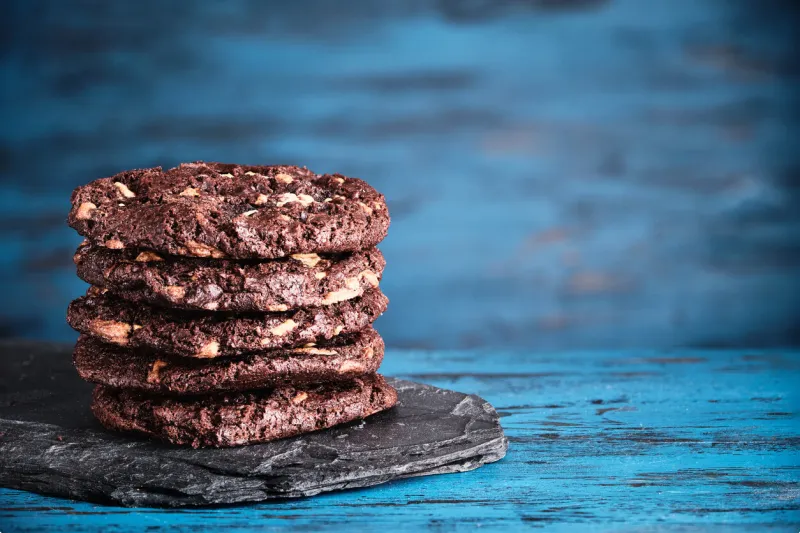 stack of chokolate cookies with cocoa, chocolate and hazelnuts on blue wooden background