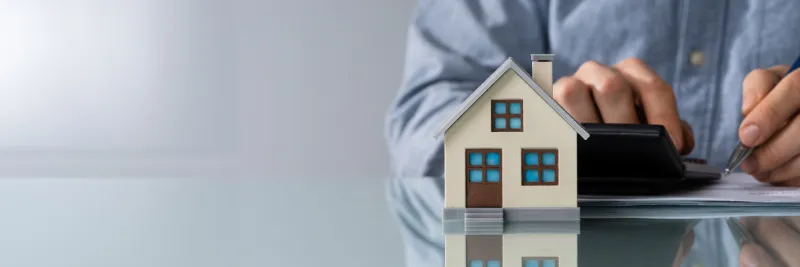 close-up of a person hand doing property tax calculation using calculator of house model