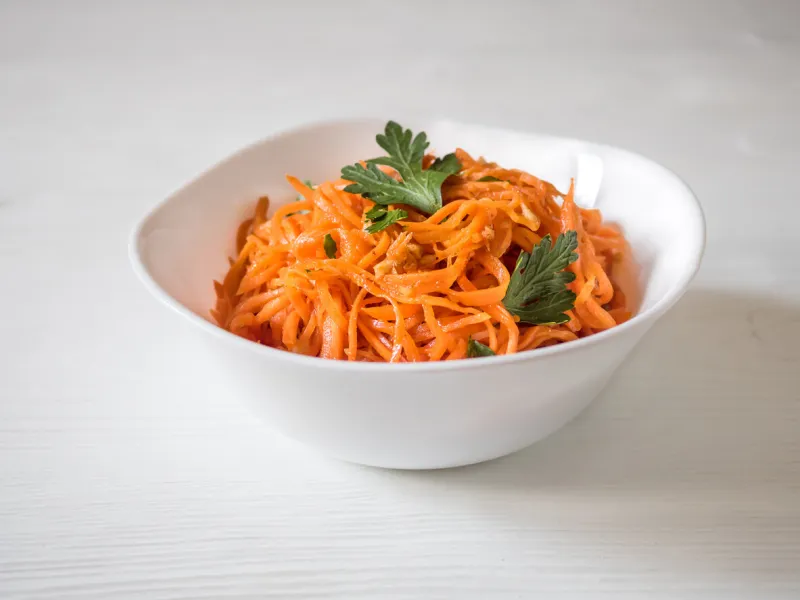 spicy asian salad with grated carrots and parsley korean carrots in a white bowl on a white backgroung vegetarian diet healthy food concept view from above horizontal