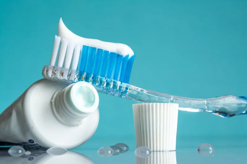 new toothbrush with toothpaste close-up in the bathroom on a mirror table with water drops on a blue background in the sunlight