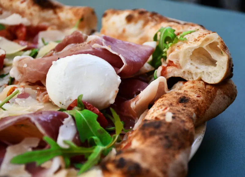 a closeup shot of freshly baked pizza with ham and herbs isolated on a dark-blue background
