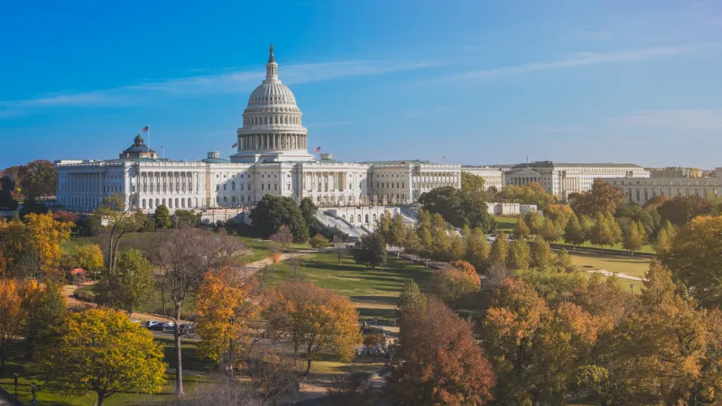 white marble domed building that serves as seat of american federal government legislative branches, house of representatives and senate with autumn trees in foreground