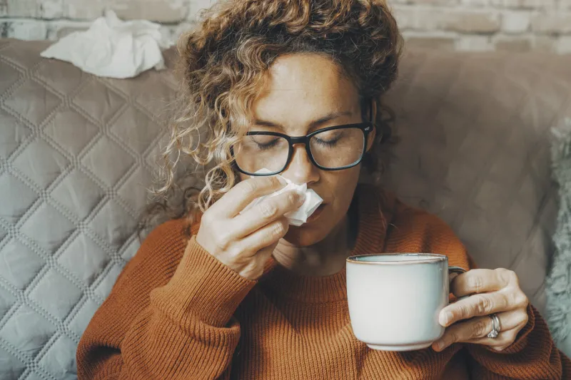 sick woman at home blowing nose and take care of influenza virus disease one female people using paper tissue and drink herbal tea medicine alone at home concept of flu cold in winter season indoor