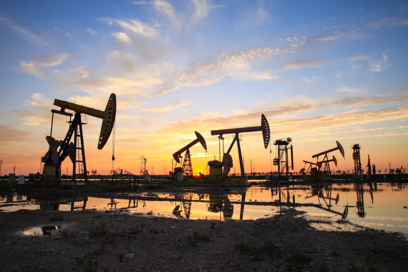 oil field site, in the evening, oil pumps are running, the oil pump and the beautiful sunset reflected in the water, the silhouette of the beam pumping unit in the evening