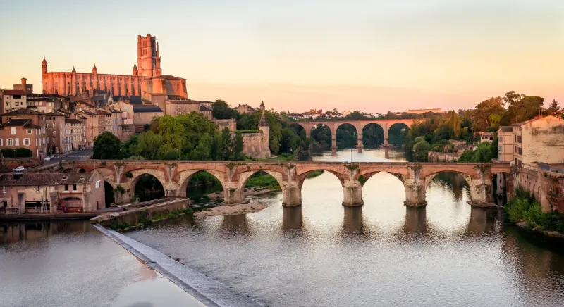 bridges across garonne river in medieval abli, france at sunrise with iconic cathedral