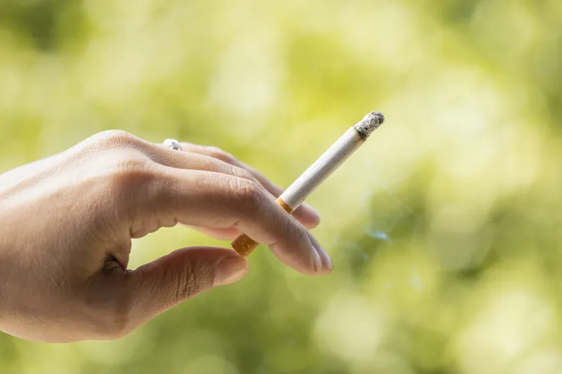 close up view of smoker holding a cigarette in hand with nature background woman with tobacco in her hand surrounded by a natural environment cigarette consumed between the fingers tobacco concept
