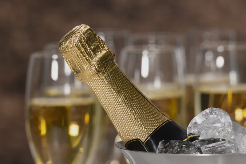 close up and selective focus of a champagne bottle neck with ice cubes with out of focus champagne glasses at the back celebration concept