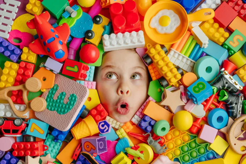 funny surprised little girl lying in the chaos of toys kid's face surrounded by building blocks