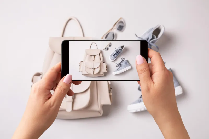 woman taking photo of white leather backpack, pastel blue sneakers and sunglasses with smartphone blogger, influencer or stylist capturing spring fashion accessories for social media