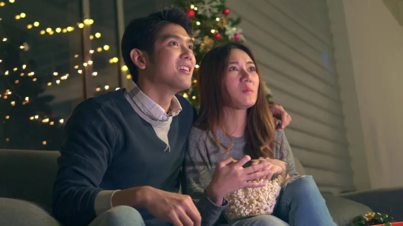 stock videona young asian couple sits on a sofa in a decorated room to celebrate christmas and new year man and girlfriend eating popcorn and enjoying to watching tv show