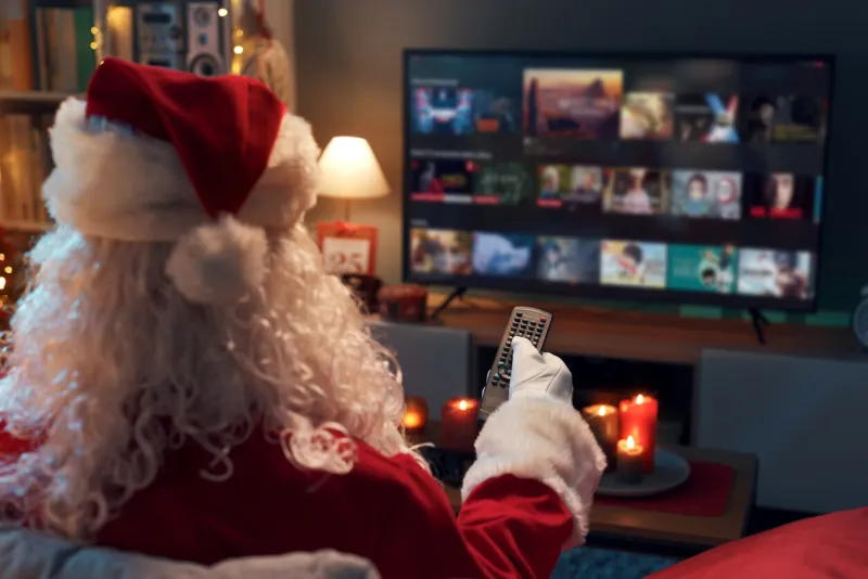 santa claus relaxing on the couch at home and watching tv, he is choosing a movie on the video on demand menu