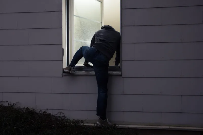 rear view of a burglar entering in a house through a window