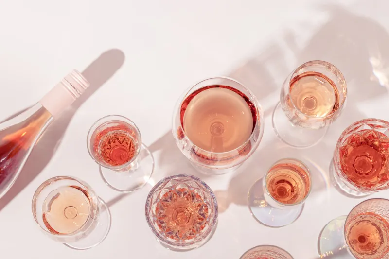 many glasses of rose wine and bottle sparkling pink wine top view light alcohol drink for party flat lay on light table at summer day with shadows