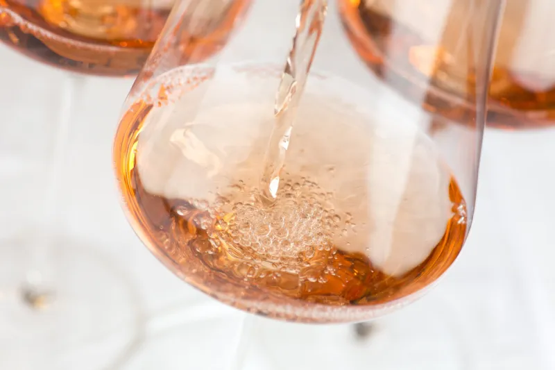 pouring rose wine in a glass in front of white background