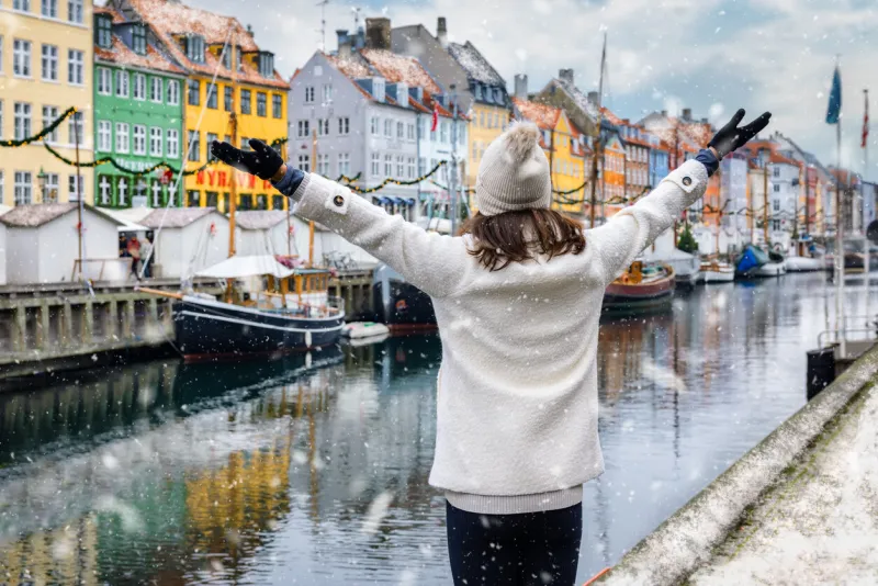 a happy tourist woman enjoys the view to the beautiful nyhavn area in copenhagen, denmark, during winter time with snow and christmas decorations