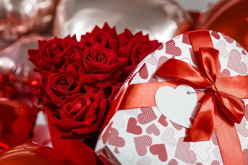 valentine's day red roses in a white box in the form of a heart on the background of foil balls a gift for women on a holiday the concept of delivering flowers floristry and flower shops