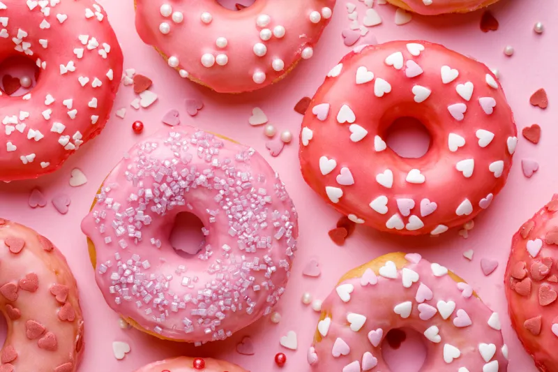 sweet donuts with pink glaze decorating sprinkles on a pink background, top view