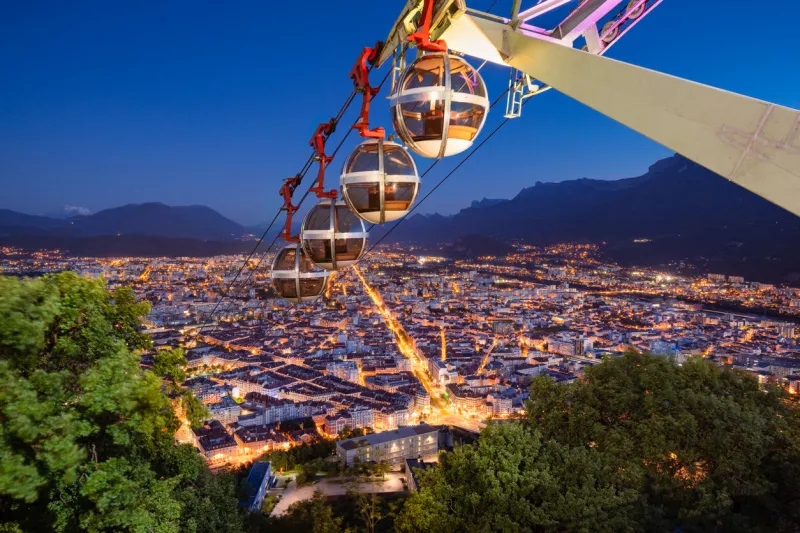 grenoble, isere, france - may 15, 2022  grenoble-bastille cable car (known as les bulles) with elevated view of the city of grenoble in evening one of the oldest cable cars in the world (built 1934)