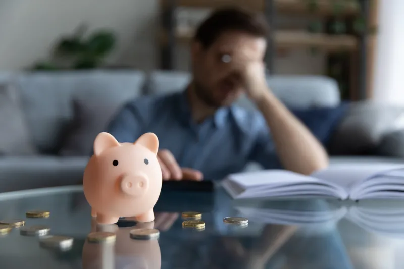 close up focus on piggybank on table, young man feeling stressed calculating expenditures or taxes, managing future payments or planning investments, suffering from lack of money, accounting concept