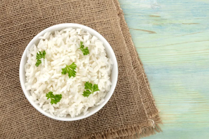 a photo of a bowl of cooked white long rice, shot from the top on rustic textures with copy space