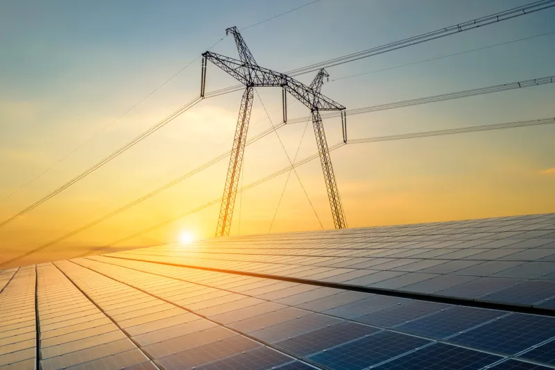 high voltage pylons with electric power lines transfering electricity from solar photovoltaic sells at sunrise production of sustainable energy concept