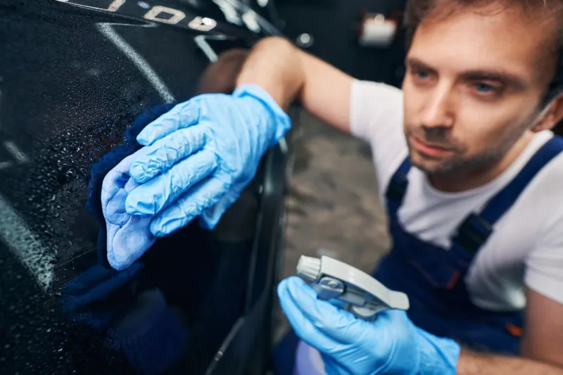 focused male auto mechanic removing dirt from car autobody with degreaser and wiping cloth